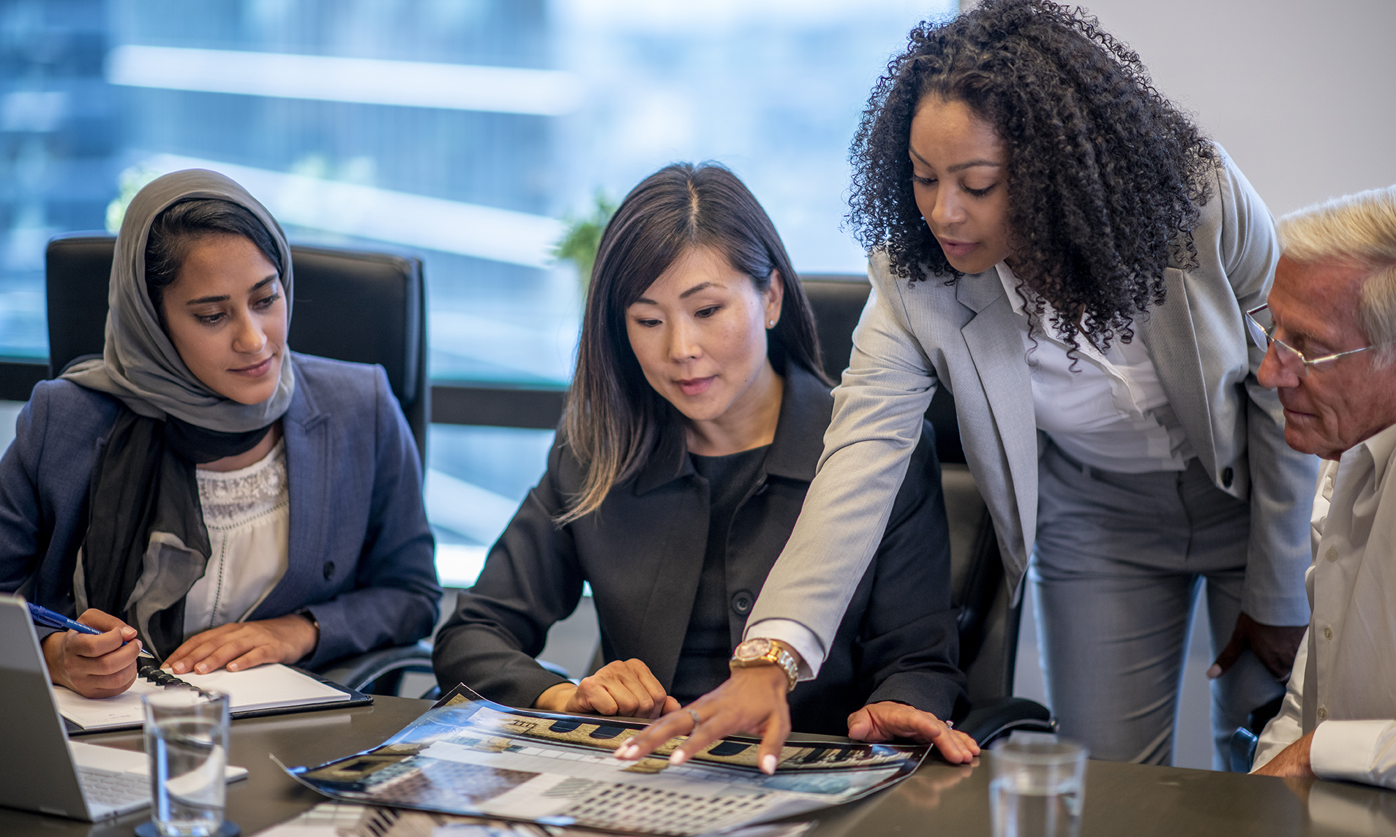 Four business people look at a photo on a table.
