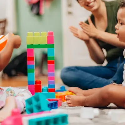 Children playing with building blocks at a day care centre with a caregiver clapping in the background