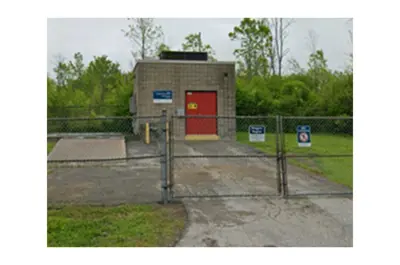 The Shirley Road Sewage Pumping Station behind a chain-link fence. It has a grey brick exterior and a red door.