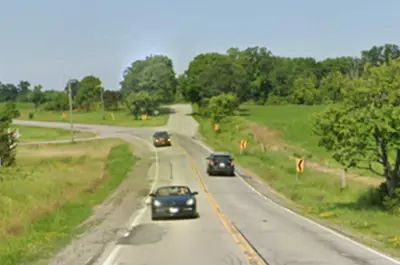 Cars drive down Twenty Mile Road on a sunny day