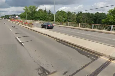 A car drives across Hydro Canal Bridge on Lundy's Lane (Regional Road 20). There are potted flowers on the median.