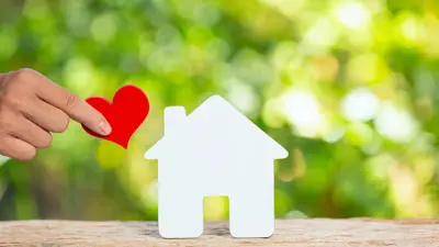 Hand holding a red paper heart next to a white paper house cut out