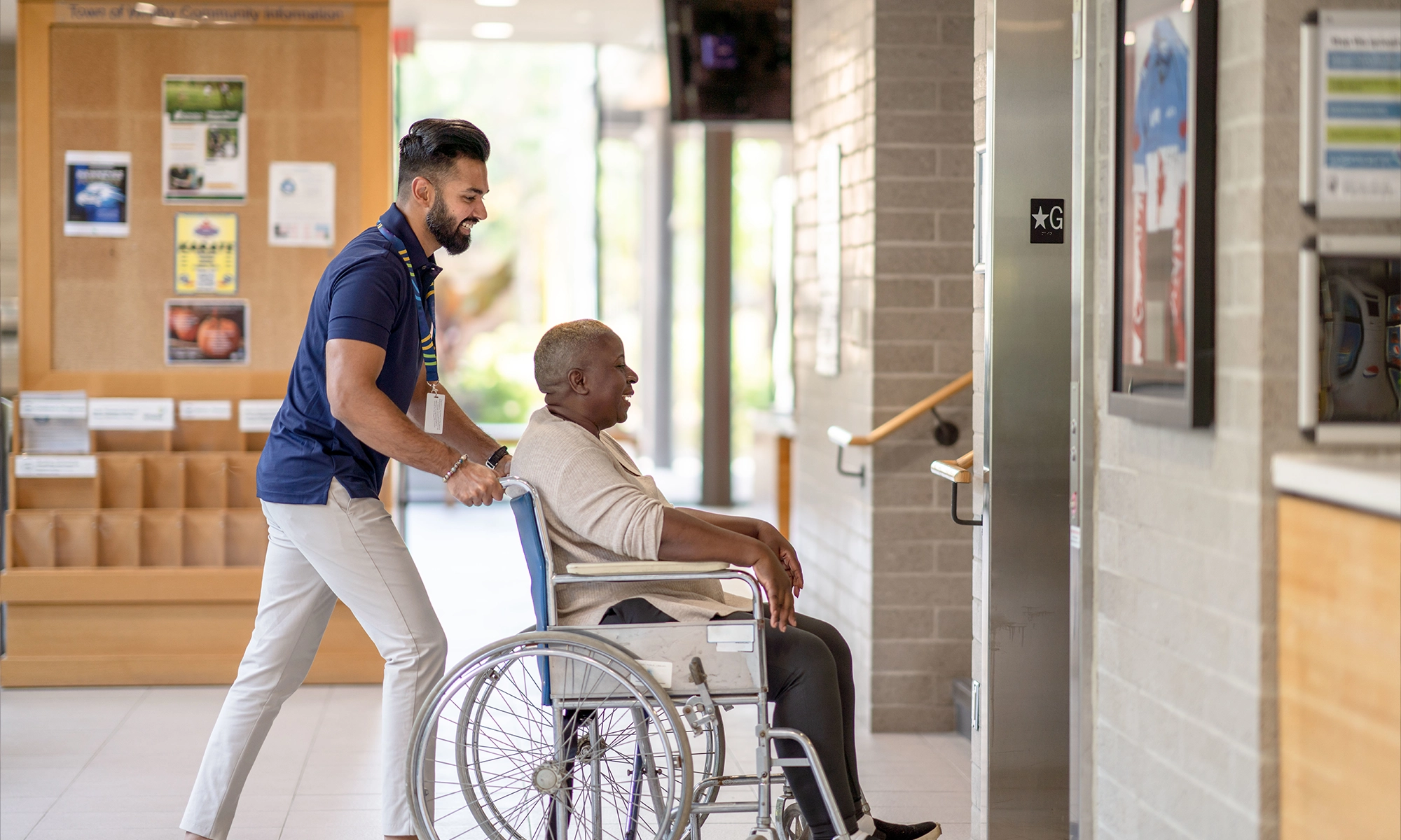 Caregiver pushing a man in a wheelchair indoors