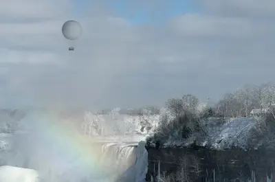 A hot air balloon floats above a snowy landscape and rainbow in Niagara Falls