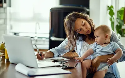 Mother holding baby while reviewing bills on a computer