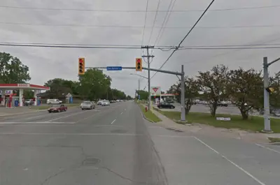 McLeod Road at Dorchester Road looking east. There are cars on the road, traffic lights, and an Esso station on the left