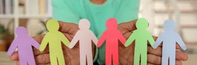 Soft focus of woman in background holding up colourful paper cutouts of people joined by their hands.