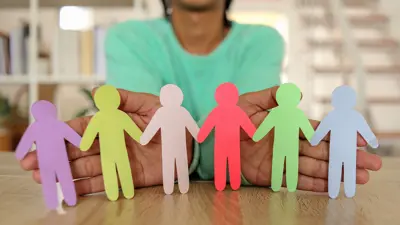 Soft focus of woman in background holding up colourful paper cutouts of people joined by their hands.