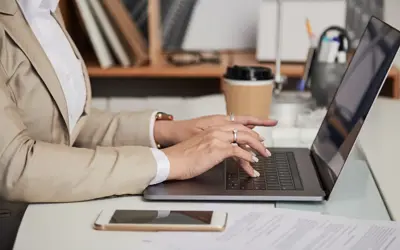 Woman typing on a laptop with a coffee and phone next to her.