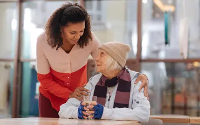 A woman giving support and a glass of water to a senior in need of help