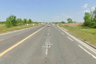 Lyons Creek Road is surrounded by grass and trees on its left and right