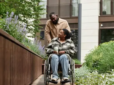 Smiling man assisting partner in wheelchair outdoors