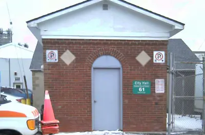 City Hall Sewage Pumping Station is a small brick building with a grey door. A truck with pylons is parked outside