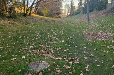 A sewer cover for the Portage Trunk Sewer sits on a grassy field surrounded by trees