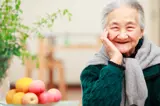 Older Asian woman smiling with a bowl of apples